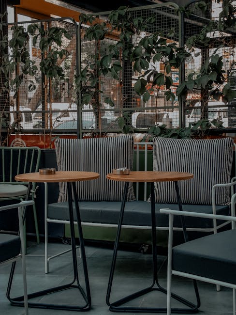 Indoor seating area at a cafe on Barnes High Street featuring a black cushioned bench with striped fabric upholstery and a wooden backrest, paired with matching black chairs with wooden arms. In front