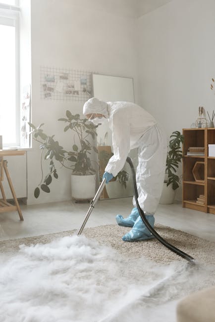 A person kneeling on a patterned carpet in a residential setting is opening a yellow and black vacuum cleaner, which is positioned on the floor. The individual is wearing blue jeans and a beige top, a